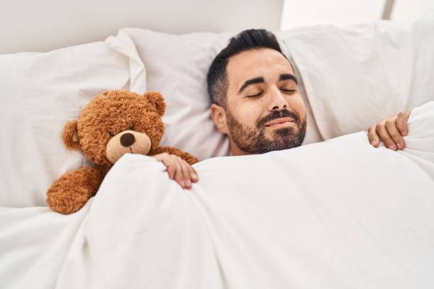 istock Young hispanic man lying on bed sleeping with teddy bear at bedroom 1437943912