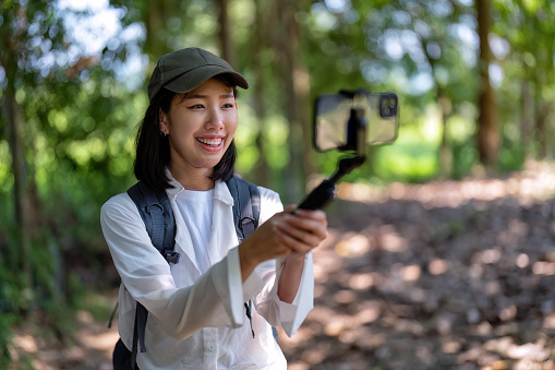 Young backpack hiking woman walking in the forest use mobile phone video call live streaming