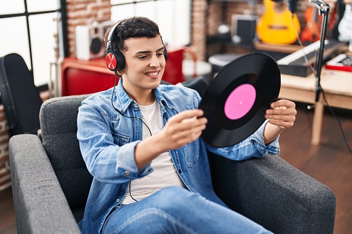Young non binary man musician listening to music holding vinyl disc at music studio