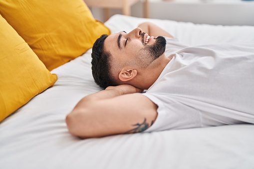 Young arab man relaxed with hands on head lying on bed at bedroom