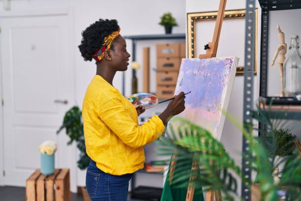 joven artista afroamericana sonriendo dibujando confiada en un estudio de arte - art university studio domestic room fotografías e imágenes de stock