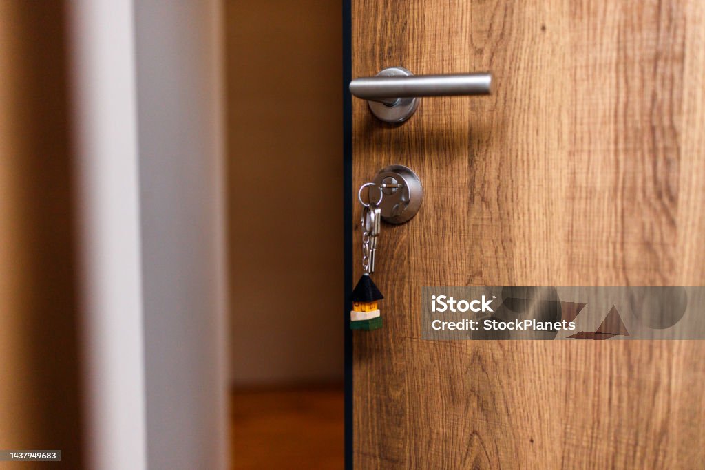 Open door and door handle with a key and a keychain shaped house Close-up of open door and door handle with a key and a keychain shaped house. Door Stock Photo