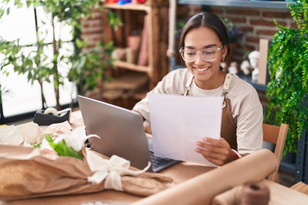 istock Young beautiful hispanic woman florist using laptop reading document at florist 1437951280