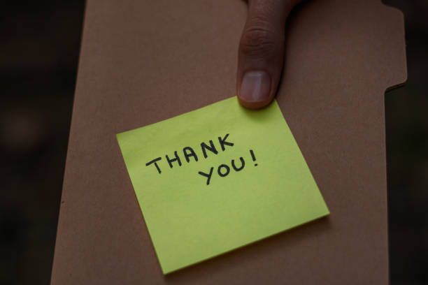 istock Close up on a brown notebook with a post it note saying thank you glued on the cover held by a hand 1437952735