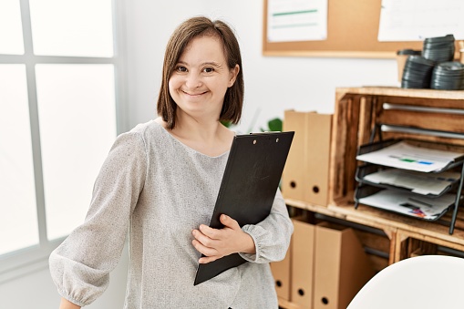 Brunette woman with down syndrome working holding clipboard at business office