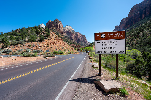 Aerial view overlooking a straight road and epic mountains in the Zion National Park, Utah, USA. A road sign showing direction and distance to Zion Canyon and Bryce Canyon.