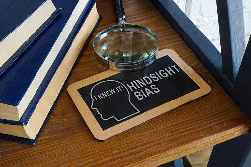 Hindsight bias inscription on the plate and a magnifying glass.