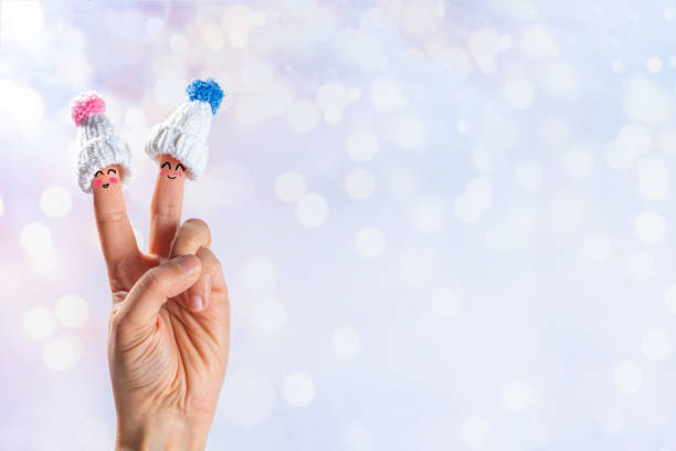 Funny cartoon fingers characters in hats. Fingers with happy faces in winter hats on snowy festive lights background copy space. Christmas vacation, family time celebrating concept, banner format