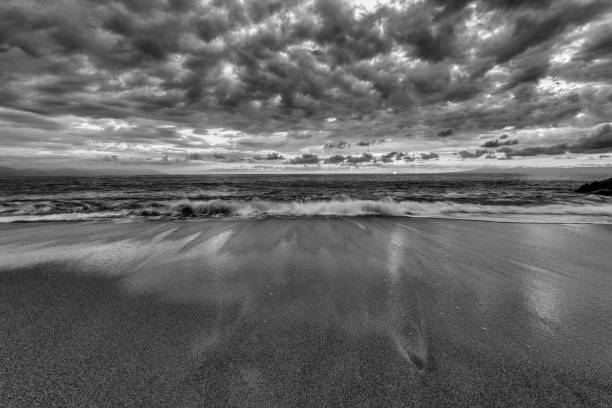 Black and white landscape of sunrise over the ocean waves and sandy beach