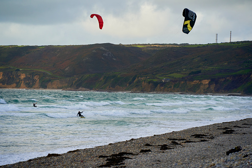 France, Vauville - October 07, 2022: Kiteboarding with Ozone reo kite on the water. 2 water sportsman between waves in front of mountain landscape. France, Normandy, Manche, Vauville.