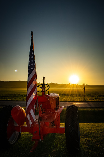 A vintage red tractor on a hazy sunrise with American flag displayed