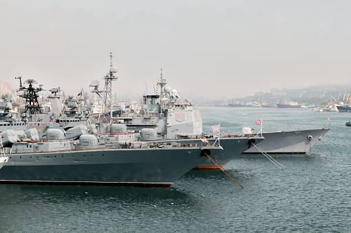 Three Russian destroyers ride at anchor in the harbor at Vladivostok in the late afternoon with a hazy background. This is the headquarters of the Russian Pacific Fleet.