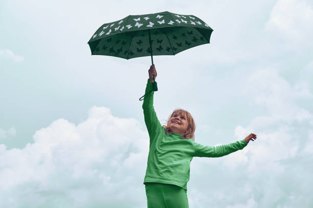 une fille de 10 à 11 ans vole sur un parapluie. enfant sous un parapluie contre un ciel nuageux - 10 11 years cheerful happiness fun photos et images de collection