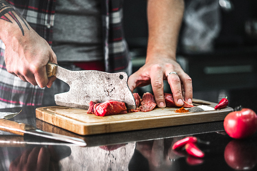 Man chopping meat with a butcher knife in the kitchen