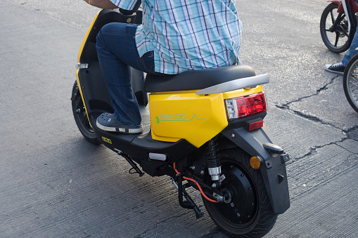 Detail of thai man on electric motorcycle. Scene is at junction in Bangkok Ladprao. Man is waiting at stoplight and is sitting on new yellow eletric motorcycle
