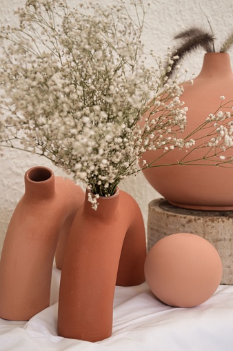 Earthenware vases of different shapes with flowers on white clothing background