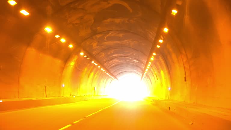 Driving in dark empty tunnel, approaching and entering dazzling light at exit. Windshield point of view, ungraded.