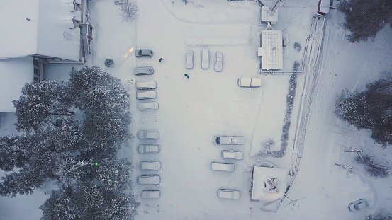Aerial top view of snow covered house, parked cars and green pine trees in winter time. Empty yard in frosty winter weather.