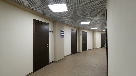 Empty, round corridor with light beige walls and closed, dark brown doors. Closed doors along a lighted corridor in the office building