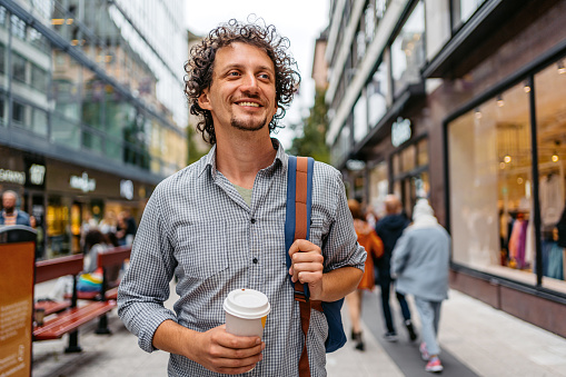 Handsome young man walking in town square in Stockholm, Sweden and drinking coffee.