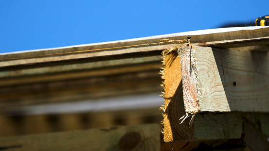 Close up of roofing wooden construction with a nail and a tight rope around it on blue sky background. Rough wooden boards and roof covering white cloth swaying in the wind.