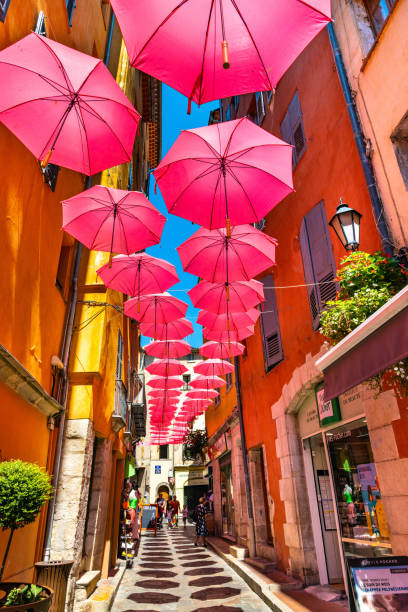 Historic tenement houses and narrow streets with pink umbrellas of old town of perfumery city of Grasse in France stock photo