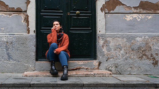 Woman sitted in the street, looking to the side  with the hand on the chin