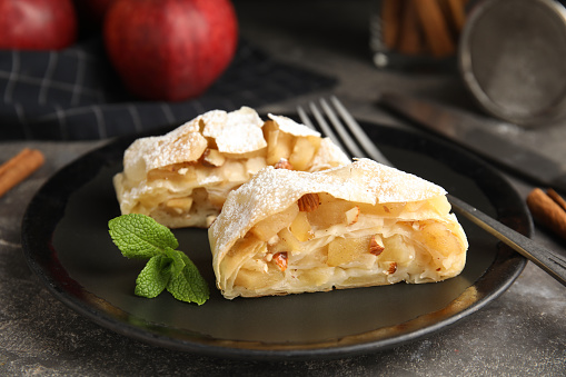 Delicious apple strudel with almonds, powdered sugar and mint on grey table