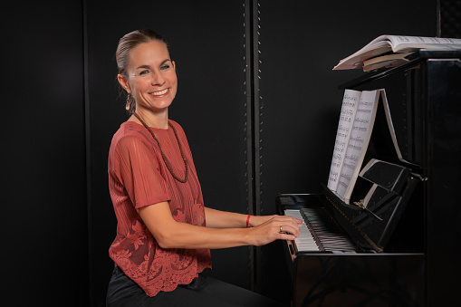 Beautiful woman sitting at the piano in dark room and smiling at camera