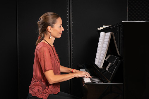 Beautiful woman sitting at the piano in dark room and smiling at camera