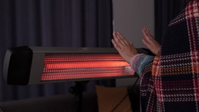 Person heating their hands at home over a domestic portable radiator in winter
