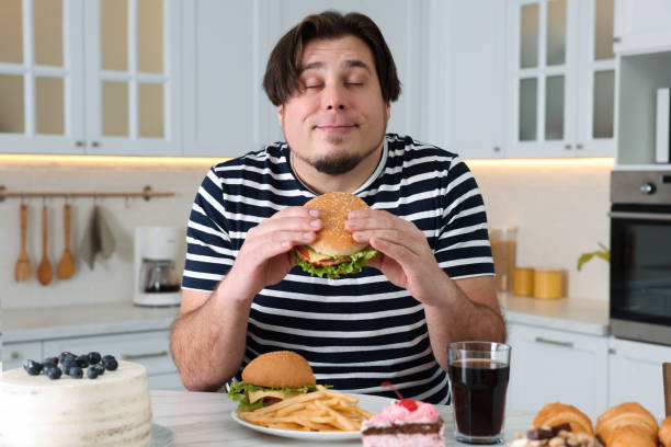 istock Happy overweight man with tasty burger at table in kitchen 1437983793