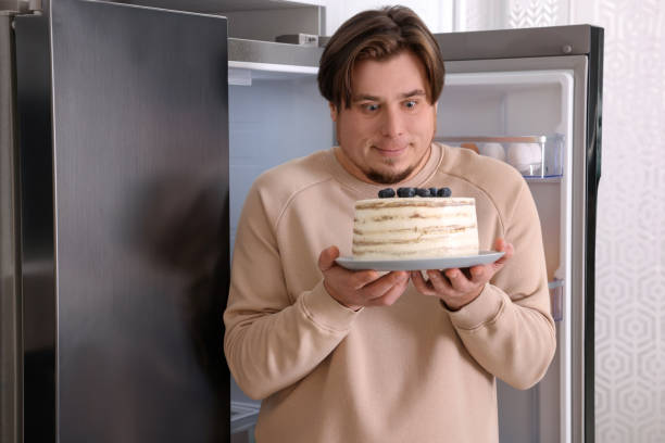 istock Happy overweight man with cake near open refrigerator in kitchen 1437983892
