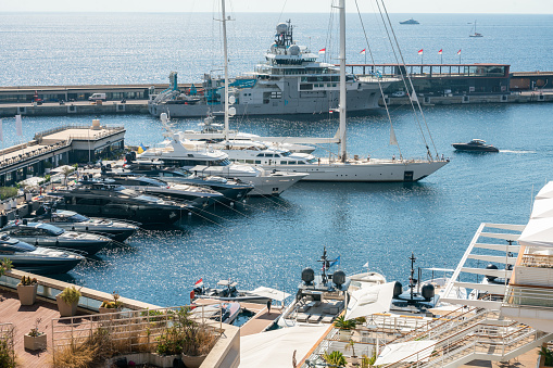 A fantastic huge sailboat(maybe it is sport boat) in the harbor of Monaco and a speed boat moving on the open sea, as well as other ships, boats and people at a great distance.  Photo from the Monte Carlo area.