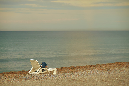 Bright light. Picture of a person sitting on the beach at sunset on a chair. Calm sea