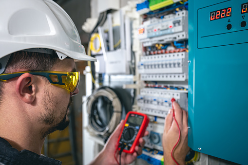 Man, an electrical technician working in a switchboard with fuses. Installation and connection of electrical equipment. Professional uses a tablet.