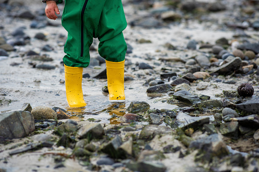 Jumpsuit and rubber boots, best outfit to go and play on the beach on a rainy day. Half toddler body wearing green jumpsuit and yellow rubber boots