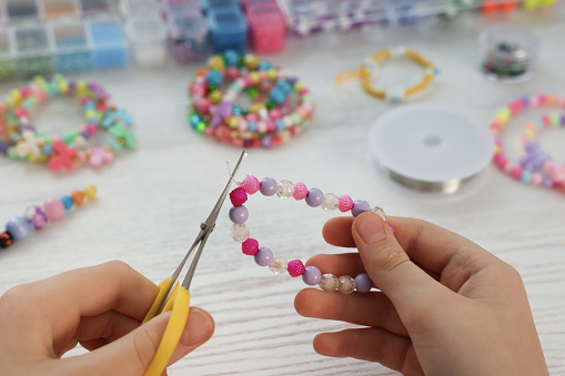 Girl making beaded jewelry at white wooden table, closeup