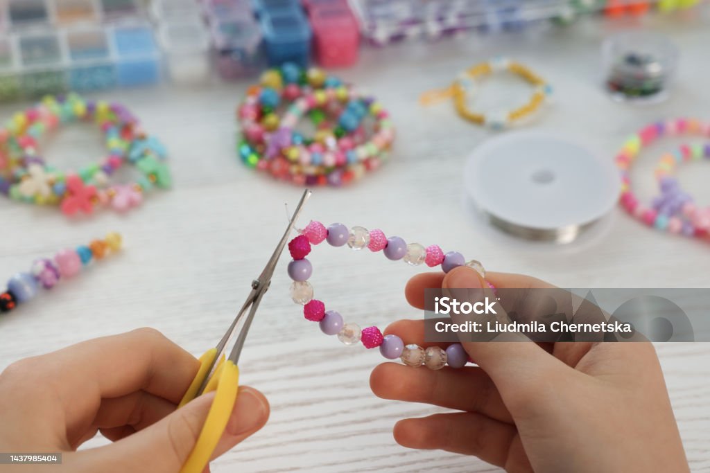 Girl making beaded jewelry at white wooden table, closeup Bracelet Stock Photo