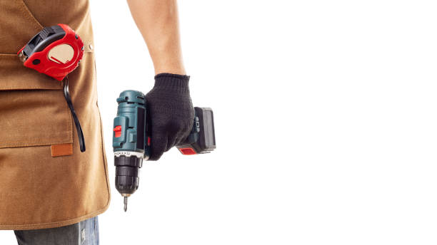 istock Man in apron and gloves holds cordless screwdriver on white background 1437985532