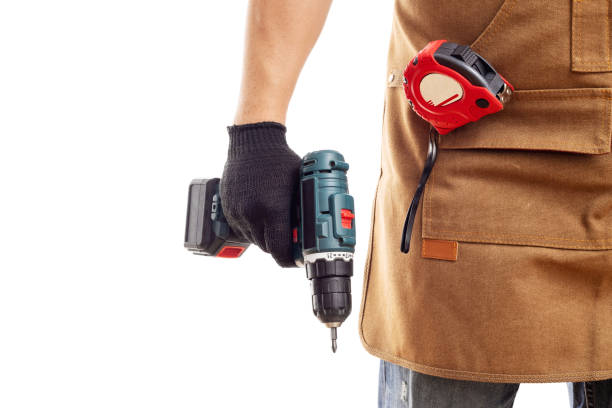 istock Man in apron and gloves holds cordless screwdriver on white background 1437985541