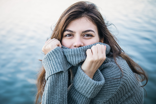 Attractive young woman in a sweater on the background of the sea, expressive look, cold season.