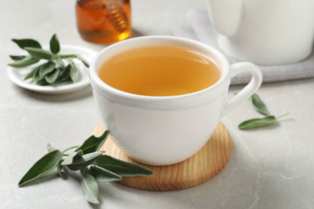 istock Cup of aromatic sage tea and fresh leaves on light grey table 1437987763