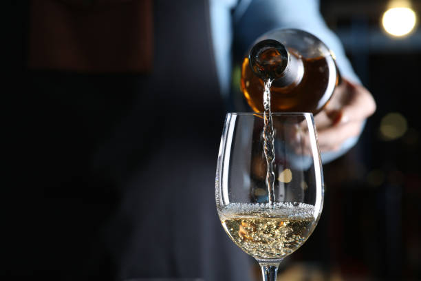 barman versant du vin blanc de la bouteille dans le verre à l’intérieur, gros plan. espace pour le texte - renverser photos et images de collection