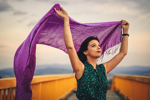 Beautiful young woman with a purple scarf outdoors on the bridge.