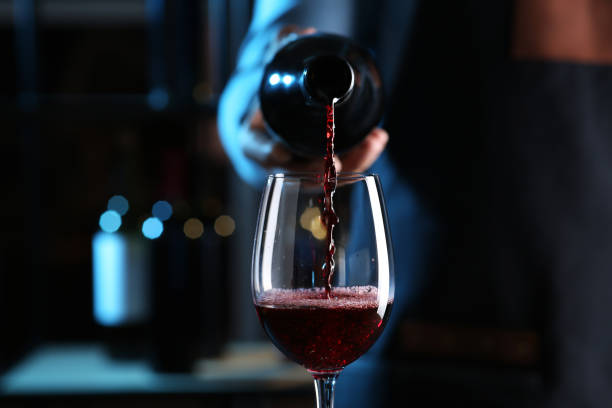 barkeeper gießt rotwein aus der flasche ins glas drinnen, nahaufnahme - wine wineglass red wine pouring stock-fotos und bilder