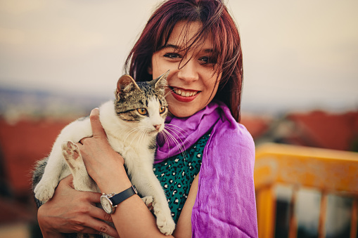 Beautiful young woman holding a cat outdoors.