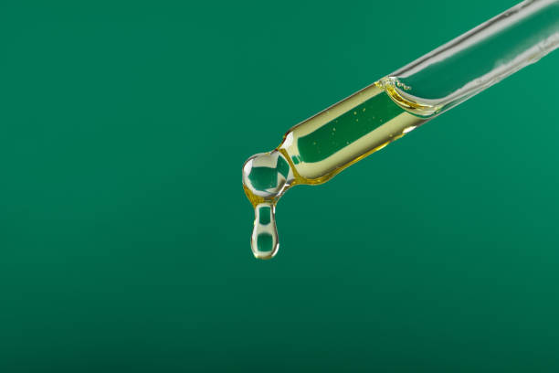 istock Dripping hydrophilic oil from pipette on green background, closeup. Space for text 1437988734