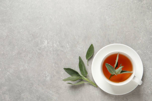 istock Cup of aromatic sage tea and fresh leaves on grey table, flat lay. Space for text 1437989319