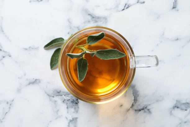 istock Cup of aromatic sage tea with fresh leaves on white marble table, top view 1437989698